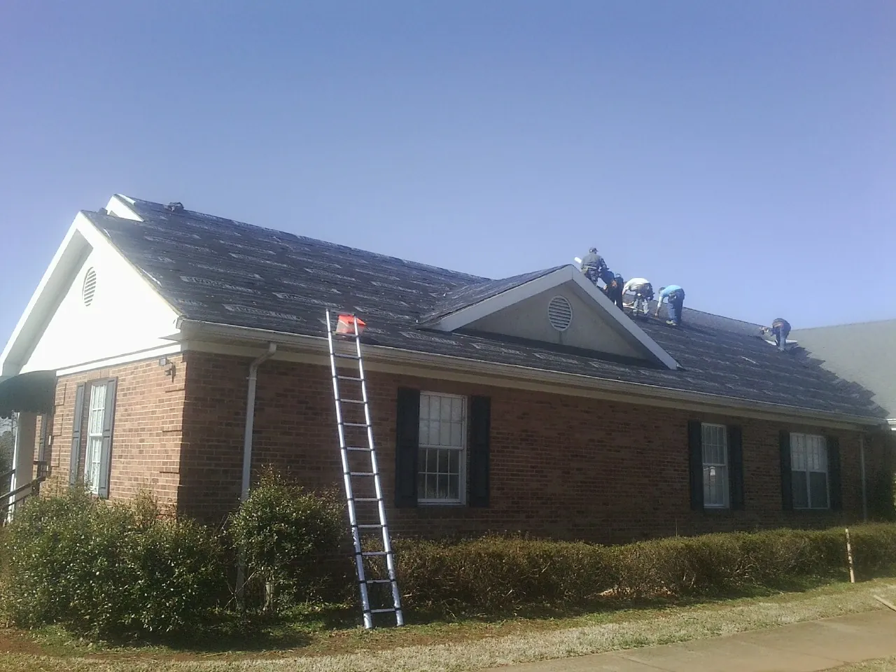 Crew tearing shingles off a brick ranch roof with a ladder set — Metal Roof Repair work by our crew in Leipsic