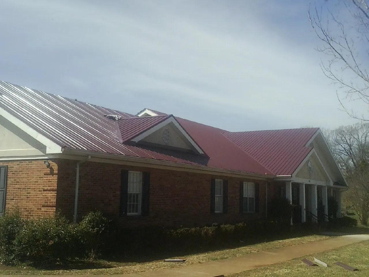 Red metal roof with gabled entries on a long brick building, from a Hail Damage Roof Repair job in Leipsic