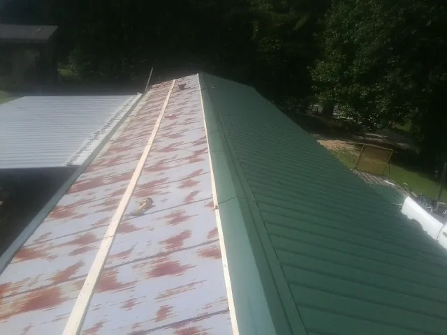 Old rusted panels beside newly installed green metal roofing — Wind Damage Roof Repair by Roofing Brothers in Leipsic