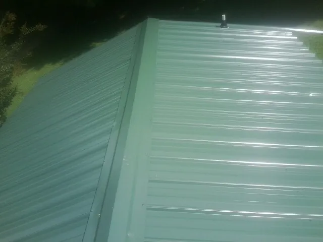 New green metal panels meeting at the ridge of a roof — Flat Roof Repair work by our crew in Leipsic