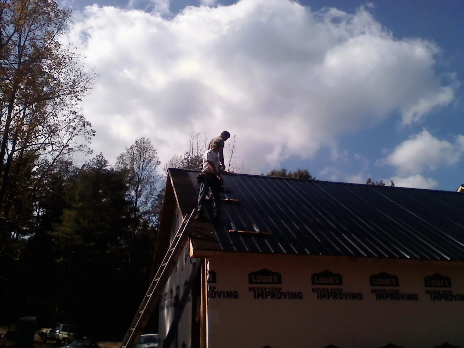 Roofer fastening dark metal panels high against a cloudy sky, from a Roof Inspection job in Leipsic