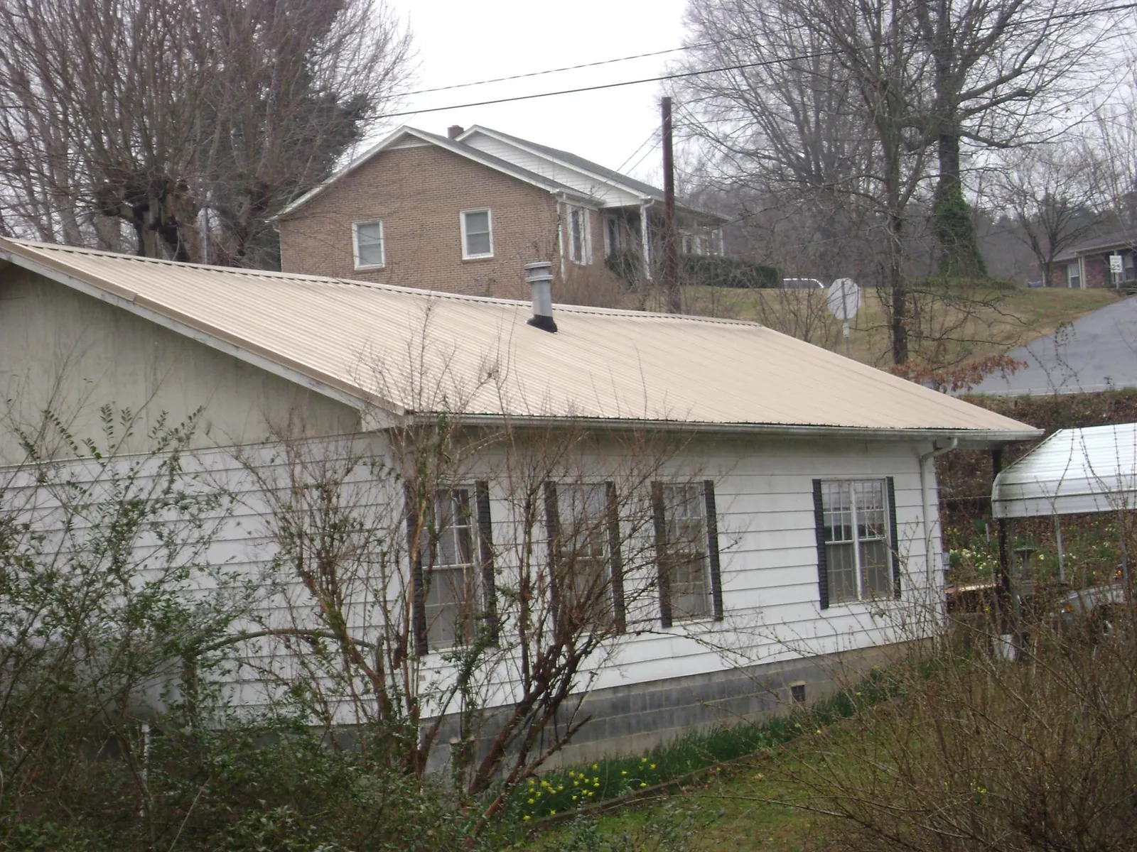 Tan metal roof on a white sided house set into a hillside — Commercial Roofing by Roofing Brothers in Leipsic